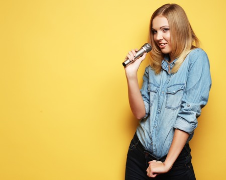 Portrait of a charming blonde woman singing with microphone in studio over yellow background.の写真素材