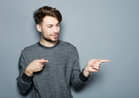 a young and handsome businessman pointing up with his finger over grey backgroundの写真素材