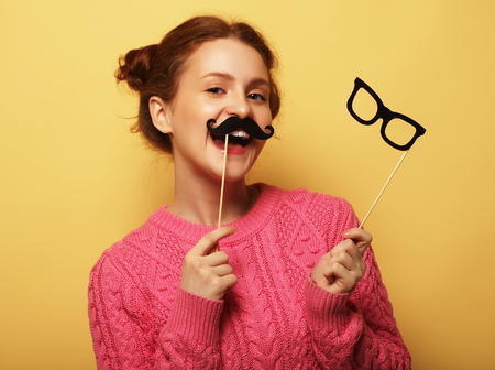 Young woman with  fake mustaches and glasses over yellow backgroの写真素材