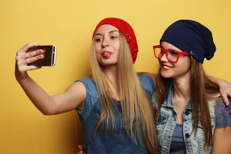 Happy girls  with smartphone  over yellow background. Happy self