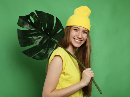lifestyle, emotion and people concept: Young beautiful woman wearing yellow casual clothes, holding leaf of monsteraの写真素材