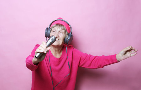 lifestyle and people concept: Funny old lady listening music with headphones and singing with mic