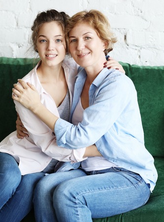Beautiful senior mom and her adult daughter are hugging, looking at camera and smilingの写真素材