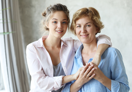 Beautiful senior mom and her adult daughter are hugging, looking at camera and smilingの写真素材
