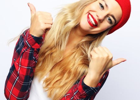pretty young hipster blonde woman with bright sexy make up wearing stylish urban plaid shirt and red hat, white background.の写真素材