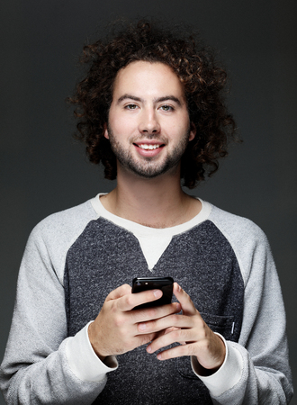 Smiling young man holding smartphone and looking at it.の写真素材