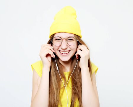 Fashion pretty cool girl in headphones listening to music wearing yellow hat  and t-shirt over white backgroundの写真素材