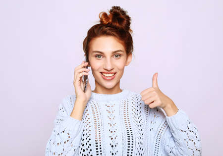 lifestyle and people concept: Portrait of a satisfied casual girl holding mobile phone and showing ok gesture isolatedの写真素材