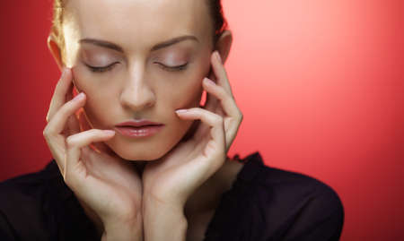 Young blond woman posing with closed eyes over red backround, beauty and fashion conceptの写真素材