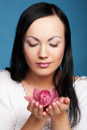 Young beautiful woman with pink orchid over blue backgroundの写真素材