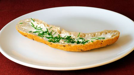 Bread roll with cheese and chives on white plate with red-purple backgroundの写真素材