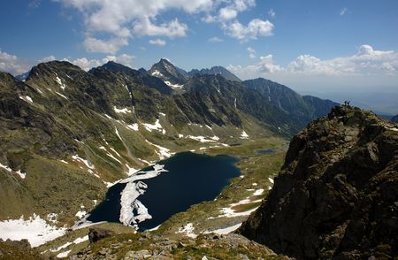 Tourists on a peak in summer day with mountain lake in valleyの写真素材