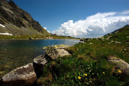 Mountain lake and green grass on plateau in sunny summer day with some clouds on horizonの写真素材