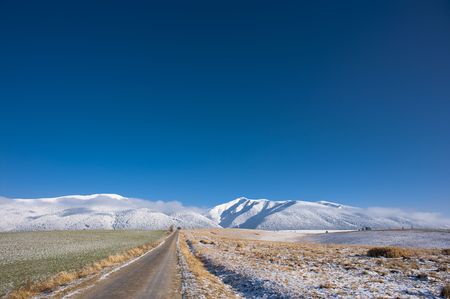 Field road in the begining of winter whit snow covered mountains in background and big blue skyの写真素材