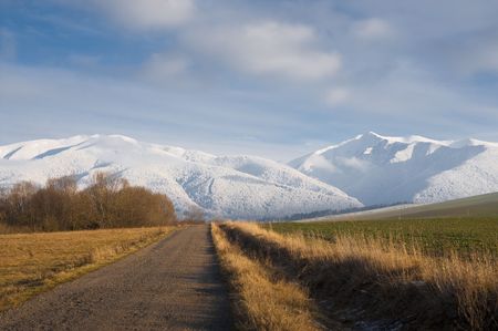 Field road in the beginning of winter whit snow covered mountains in backgroundの写真素材