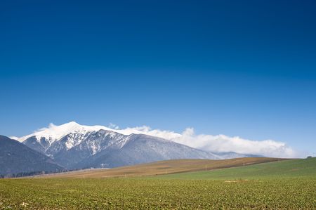 green field in sunny winter day with mountains in backgroundの写真素材