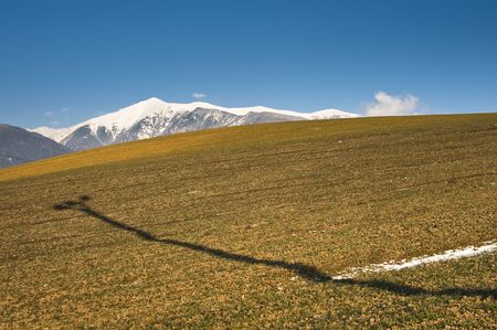 shadow of a electric pole on a field with mountains in backgroundの写真素材