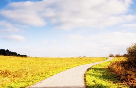veering road and horizon in autumn country, meadows an sky with cloudsの写真素材