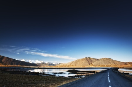 A road over bay in sunny day with mountains in the background and dark blue skyの写真素材