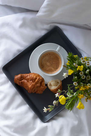 breakfast in bed, tray with cup of coffee, french fresh croissant and flowers in the morning, white bedding in the hotel room. top viewの写真素材