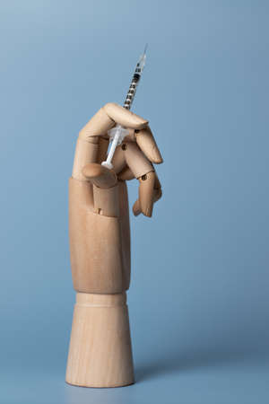 dummy wooden hand holds syringe with vaccine or medication on a blue background. insulin injectionの写真素材