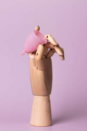 dummy wooden hand holds menstrual cup on a pink background. women healthcare during the menstruation periodの写真素材