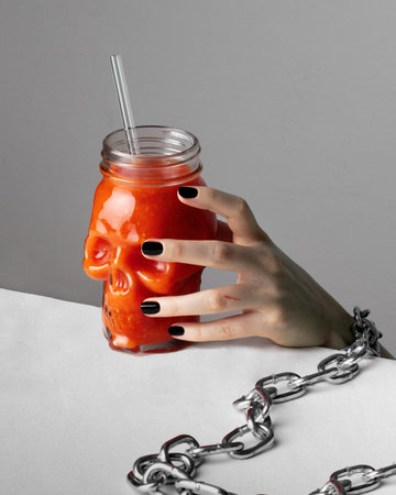 halloween concept - close-up of a womans hand in chains reaching a glass of bloody juice in the...