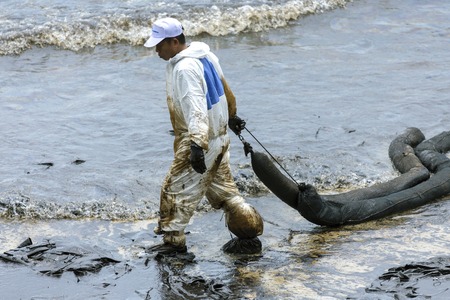 RAYONG, THAILAND - JULY 31, 2013: A Worker in biohazard suits  used Oil Containment boom as cleaning crude oil spilled from the beach of Samet Island on July 31, 2013 in Rayong, Thailand.のeditorial素材