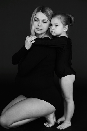 A portrait of beautiful pregnant mother with her little daughterirl dressed in black tights against dark background.の写真素材