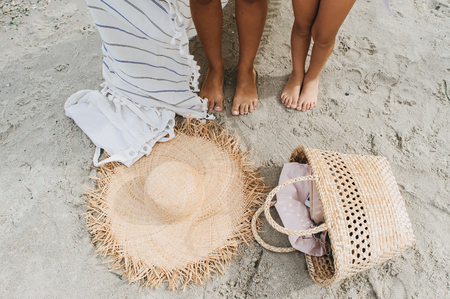 Women legs, Straw hat, bag lei garland of white sand on a sea beach.の写真素材