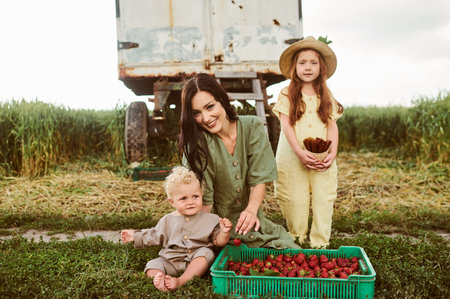 Beautiful young caucasian mother with her children in a linen dress with a basket of strawberries...