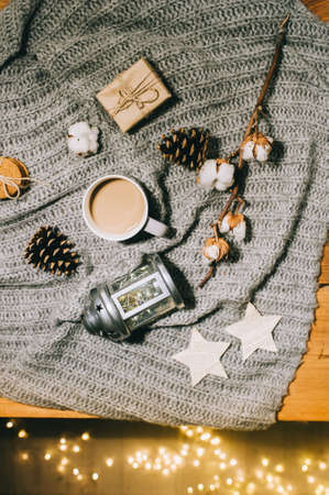 Flat lay. Cup of coffee, a branch of cotton, a candlestick and cones on a gray knitted plaid.の写真素材