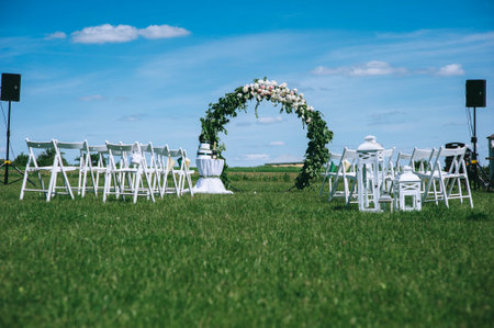 Round wedding arch decorated with peonies and greenery with white armchairs for guests outdoorsの写真素材