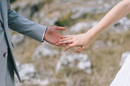 Close up of wedding couple holding hands outdoors. Blurred background.