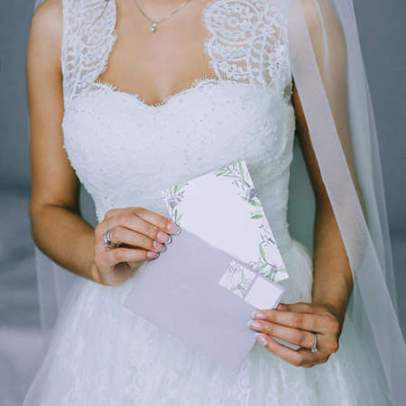 Close up of faceless girl in beautiful white wedding dress holding an envelope with a blank postcard.の写真素材