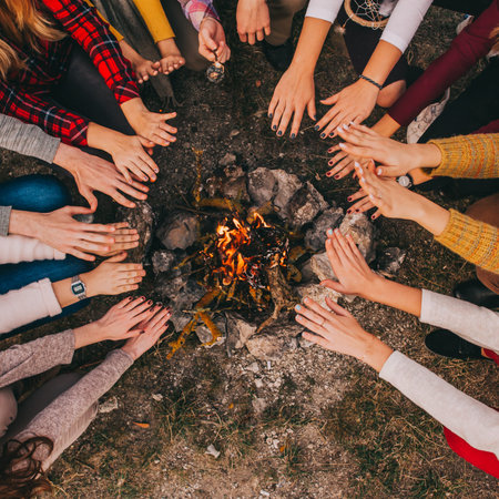 Top view of young campers sitting around and warming their hands on a campfire in the fall.