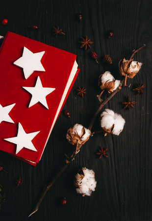 Flat lay with bright red book, white carved stars, cotton branch, and spices on a wooden background.の写真素材