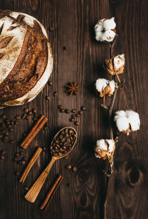 Top view of homemade bread, coffee beans and a branch of cotton wool lying on a wooden table.の写真素材