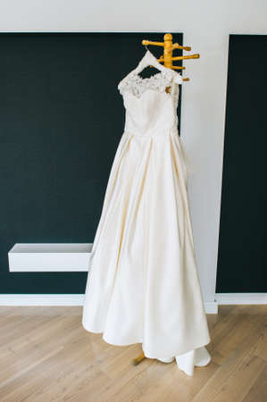 Beautiful white minimalist wedding dress hanging on a wooden hanger in the middle of the room.の写真素材