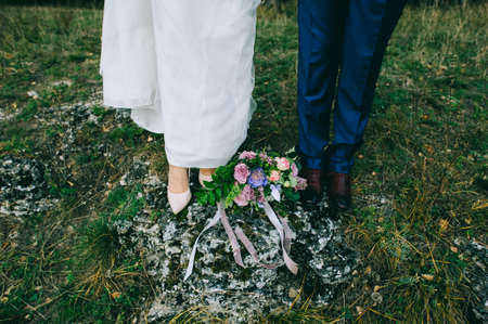 Beautiful bouquet of the bride lies on a stone at the feet of the bride and groom.の写真素材