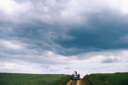 Newlyweds ride in a cabriolet in a field with poppies before a thunderstorm.