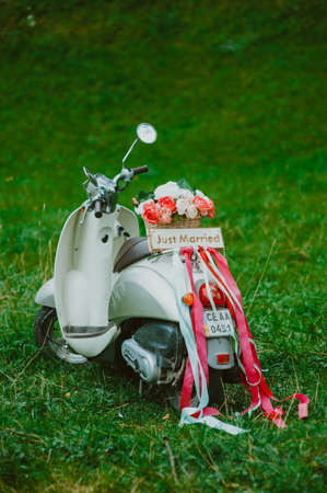 Miniature retro scooter with a basket of flowers, ribbons and a wooden board.の写真素材