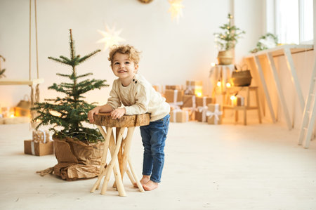 Handsome curly little boy decorated a Christmas tree in a white roomの写真素材
