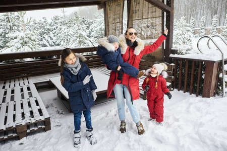 A young mother with her tree children have a fun and playing snowballs outdoor near the homeの写真素材