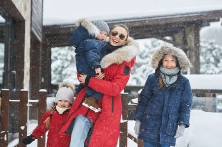 A young mother with her tree children have a fun and playing snowballs outdoor near the homeの写真素材