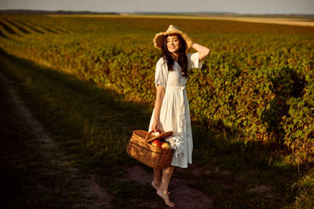 Girl in straw hat and with wicker basket on currant field background.の写真素材