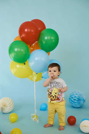 Full length portrait of cheerful boy holding balons posing against blue backgroundの写真素材