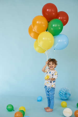 Full length portrait of cheerful boy holding balons posing against blue backgroundの写真素材