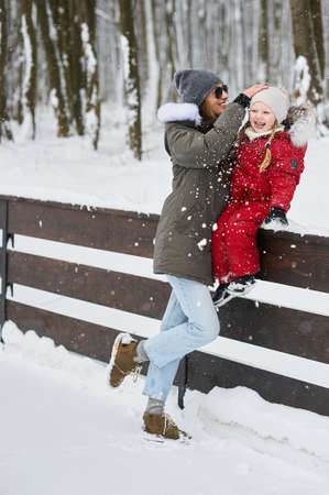 A portret of beautiful young caucasian mother with her children in winter near the house with a snow covered christmas trees in a backgroundの写真素材