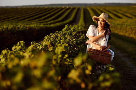 Girl in straw hat and with wicker basket on currant field background.の写真素材